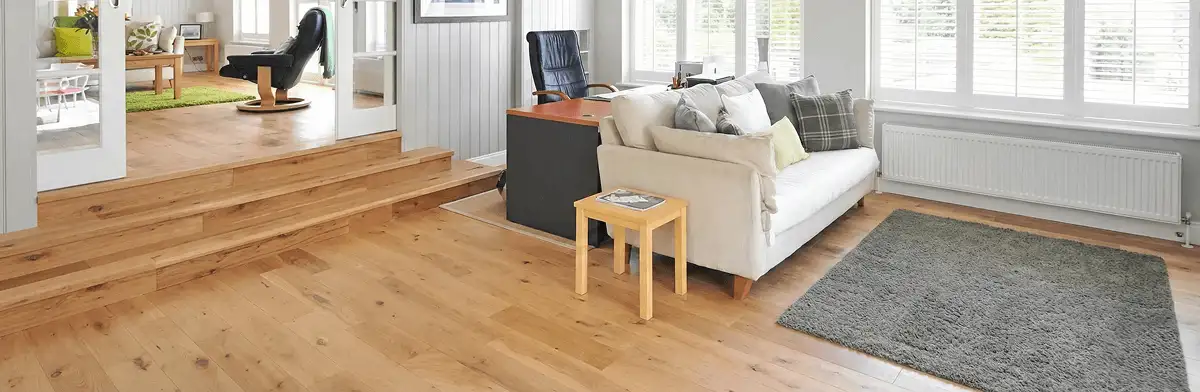 A modern living room with professionally installed laminate flooring, a beige sofa, a small side table, a gray rug, and large windows with white shutters in West Palm Beach, FL